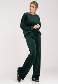 Welurowa, ciemnozielona bluza z okrągłym dekoltem i luźnym krojem, w zestawie z pasującymi dżinsami z elastycznym paskiem i sznurkiem.