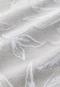 Helles beiges Gewebe mit einem dezenten, strukturierten Muster aus weißen Blättern, das ein weiches, gewebtes Erscheinungsbild erzeugt. Ideal für Polstermöbel oder Vorhänge.