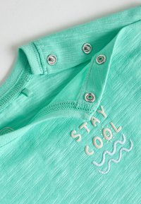 Mintgroene babyromper met drukknoopjes en geborduurde tekst "STAY COOL" boven drie golvende lijnen.