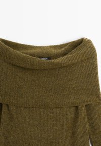 Pull en maille vert olive doux avec un col roulé large et plié et une étiquette intérieure visible.