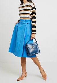 Blå plisserad kjol med bälte, randig tröja i vitt, svart och orange; bruna skor; blå handväska med cirkulär detalj som hårdvara.