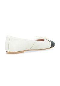 Chaussure plate blanche avec un bout noir, fabriquée en matériau doux. Présente un petit nœud à l'avant et une semelle plate et flexible.