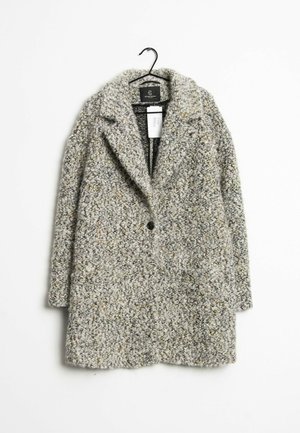 Grå tekstureret uldfrakke med brede revers og en enkelt sort knap, hængende på en sort bøjle mod en hvid baggrund.