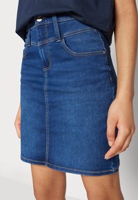 Denim skirt in medium blue with a straight cut, five-pocket design, stitched detailing, and a hem that falls above the knee.
