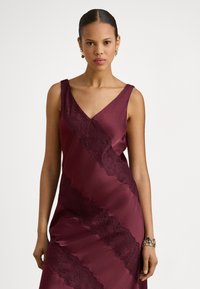 Burgundi színű szatén ruha V-nyakkivágással és átlósan elhelyezkedő csipkedíszítéssel az elején. Sima textúra, ujjatlan kivitel, testhez simuló sziluett.
