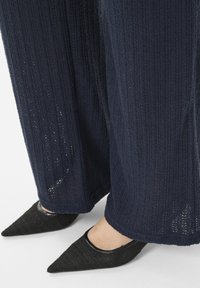 Pantalones de pierna ancha de punto en color navy con tejido texturizado; combinados con zapatos de punta negra con un brillante ribete negro.