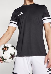 Black athletic t-shirt with white stripes on sleeves, featuring an Adidas logo. The wearer holds a patterned soccer ball with black, white, and orange accents.