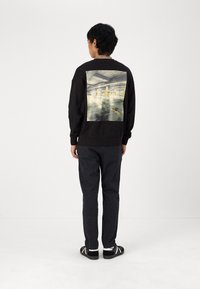 Sweatshirt preto com uma grande estampa de garagem de estacionamento urbana nas costas. Combinado com calças escuras e sapatos pretos com detalhes brancos.