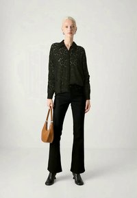 Blusa preta de renda com gola, combinada com jeans flare pretos. A modelo segura uma pequena bolsa marrom, usando botas de cano curto pretas.