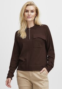 Brown long-sleeve pullover with a zippered collar, front pocket, and ribbed hem. Soft fabric with a relaxed fit. Casual design.