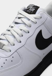 Λευκό δερμάτινο αθλητικό παπούτσι με μαύρο λογότυπο Nike, επίπεδα κορδόνια, επενδεδυμένο περιμετρικά κολάρο και λαστιχένια σόλα. Διαθέτει μαύρη ετικέτα με το λογότυπο στη γλώσσα.