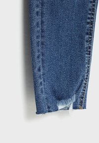 Jean en denim bleu moyen avec un ourlet déchiré et des bords effilochés. Caractéristiques de couture standard et design ajusté.
