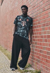Crni dres sa tirkiznim i mramornim uzorkom, sa crvenim T-Mobile logotipom. Ovaj outfit upotpunjuju široke crne hlače i sivi sportski tenisice.