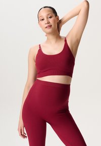 Karmozijnrode sportbeha met verstelbare bandjes en naadloos ontwerp, gecombineerd met bijpassende high-waisted leggings, met een gladde textuur.