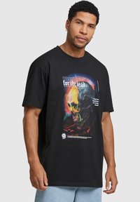 Sort bomulds t-shirt med et farverigt grafisk print af et kranium, med tekst der læser "PRAY for the dead" og et logo nederst.