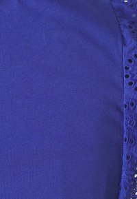 Jasně modrá látka s hladkým pleteným textura a krajkovým okrajem, který obsahuje kruhové květinové výřezy na pravé straně.