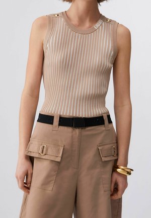 Haut sans manches beige et blanc à rayures avec détails de boutons, associé à un pantalon cargo beige et une ceinture noire, accessoirisé avec des bracelets dorés.