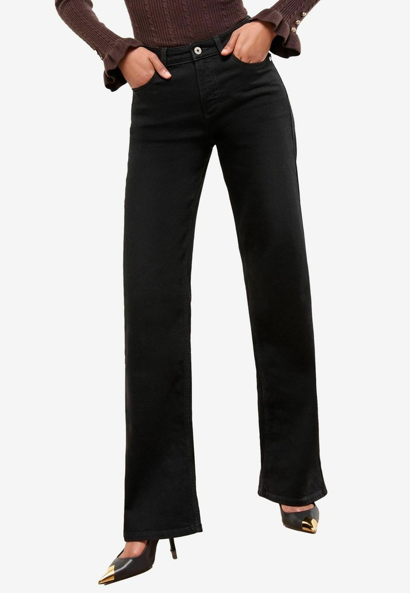 Zwarte rechtshuisdenim jeans, met voorzakken, een knoopsluiting en een klassiek ontwerp. Gecombineerd met zwarte pumps met een spitse neus.