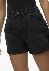 Shorts neri in denim con orlo arrotolato, tasche frontali e vita con bottone. Il tessuto ha una consistenza liscia e una leggera lucentezza.