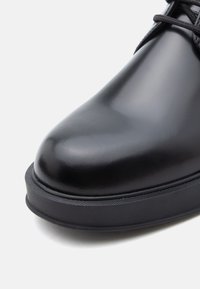 Zwarte leren schoen met een ronde neus, een gladde textuur en een rubberen zool met een subtiel profiel. Veters zichtbaar aan de bovenkant.