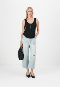 Svart ribbet tanktop med knappdetalj, lyseblå vide jeans med slitasje, og svart håndveske med tekstur. Svart hæl-sko.