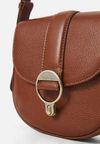 Hnědá kožená přes rameno s klopou, se zlatými kovovými akcenty a názvem značky "Barbour." Texturovaný povrch.