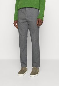 Pantalon en laine grise à coupe ajustée, avec plis plats et poches latérales, associé à des baskets vert olive. Pull en maille vert porté dessus.