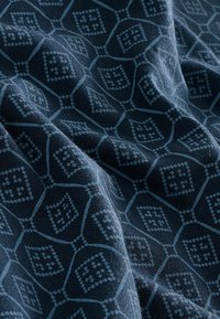 Tela azul marino con un patrón geométrico de diamantes y cuadrados en azul claro. Textura suave, con detalles en relieve a lo largo de todo el diseño.