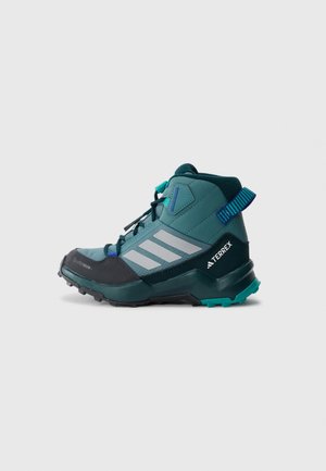 Scarpe outdoor a taglio medio di colore teal con punta nera robusta, strisce grigie e dettagli verdi. Presentano una suola testurizzata per una migliore aderenza e stabilità.