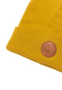 Żółta dziana czapka z wywiniętym brzegiem, teksturowana, z okrągłą, brązową skórzaną naszywką z wytłoczonym wzorem gór i niedźwiedzia.