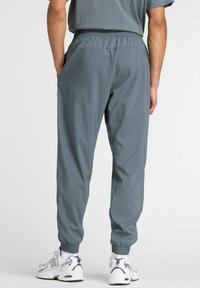 Grå joggingbukser lavet af glat stof med elastisk talje og ankelmanchetter. Båret med hvide sneakers med marineblå accenter.