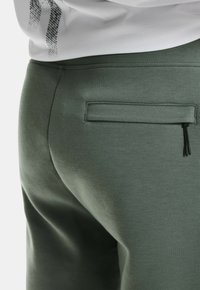 Groene joggerbroek van katoenmix met een gestructureerd oppervlak, voorzien van een klein ritszakje op de achterkant.