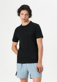 T-shirt en coton noir avec un col rond, des manches courtes et un petit logo gris sur la poitrine, associé à un short bleu clair.