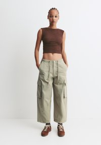 Top scurt maro din material texturat, asociat cu pantaloni cargo de culoare verde deschis, cu o croială lejeră, buzunare laterale și talie cu șnur. Încălțăminte maro.