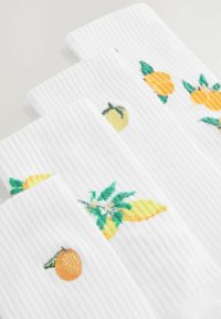 Hvide ribbede sokker med broderede frugt mønstre, herunder gule citroner, appelsiner og grønne blade, i lyse, farverige detaljer.