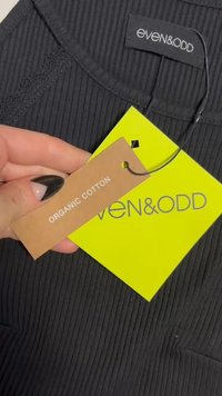 Musträpitud must kangas, millel on silt "even&ODD" ja pruun silt, mis näitab "ORGANI TICK." Sildi helekollane taust.