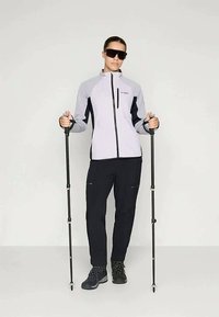 Ανοιχτό γκρι και μαύρο εξωτερικό μπουφάν με φερμουάρ, συνδυασμένο με μαύρο παντελόνι. Σκοτεινές υποδήματα και μπαστούνια πεζοπορίας ολοκληρώνουν την εμφάνιση.