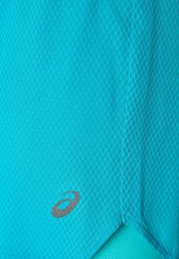 Turquoise textured athletic shirt with a honeycomb pattern; features a gray logo near the hem and clean stitching detailing.