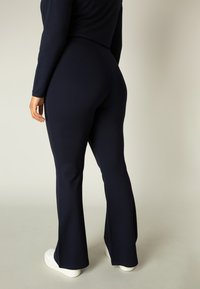 Navy flared leggings van rekbaar materiaal, aansluitend door de dijen en uitlopend vanaf de knieën, gecombineerd met witte platform sneakers.