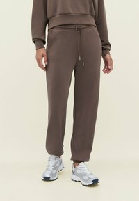 Bruine katoenen sweatpants met een elastische tailleband en trekkoord, met omslagmanchetten, gecombineerd met grijze sportschoenen met mesh accenten.