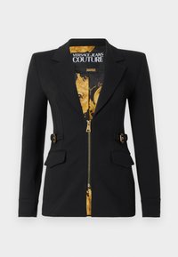 Čierne priliehavé sako s podšívkou zo zlatej barokovej vzorky, predným zipsom, výrezmi na klopách, bočnými detailmi s prackami a klopovými vreckami.