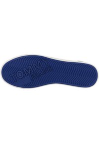 Suela de zapato de goma azul con patrón de tracción en zigzag y logo "TOMMY JEANS" grabado en letras grandes.