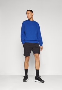 Felpa a maniche lunghe blu con collo tondo, pantaloni corti neri, calze nere e scarpe da ginnastica nere. Design semplice con minimale branding e un taglio comodo.