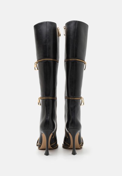 Zwarte leren laarzen tot de knie met gouden hardwareaccenten en ritsdetails, met een spitse hak en een gladde, glanzende textuur.