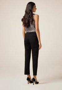 Zwarte op maat gemaakte broek met een slanke pasvorm en een taille op middenhoogte. Gecombineerd met een mouwloze top met pailletten. Zwarte hoge hakken maken de outfit compleet.