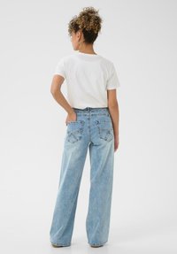 Lyseblå oversized denimjeans med højtaljet, brede ben og to baglommer. Kombineret med en tætsiddende hvid t-shirt.