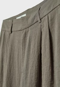 Gros plan sur un pantalon en lin beige montrant la ceinture avec passants pour ceinture et un détail plissé à l'avant.