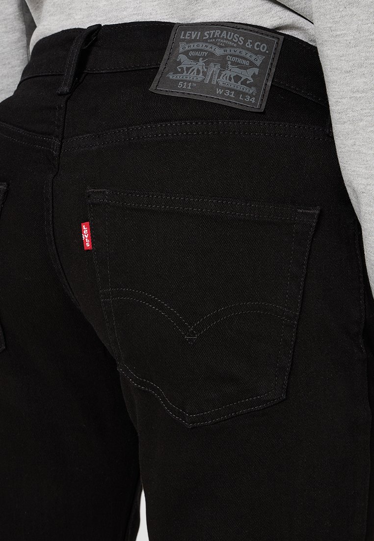 Vaqueros de mezclilla negra con un bolsillo trasero que presenta costuras curvas. La cinturilla tiene una etiqueta de cuero con la marca que indica la talla 31x34.
