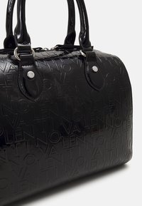 Black patent leather handbag with embossed logo pattern, rounded shape, dual handles, and silver hardware accents. Texture is glossy and sleek.