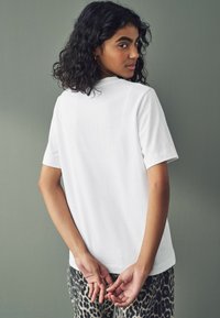 Witte t-shirt met korte mouwen en een relaxte fit, gecombineerd met lichtgevlekte broek met luipaardprint. Gladde katoen textuur en eenvoudig ontwerp.